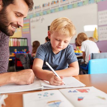 Elementary School Teacher Giving Male Pupil One To One Support In Classroom Elementary School Teacher Giving Male Pupil One To One Support In Classroom